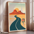 A framed poster depicting a desert landscape with a winding road leading to a motel sign.
