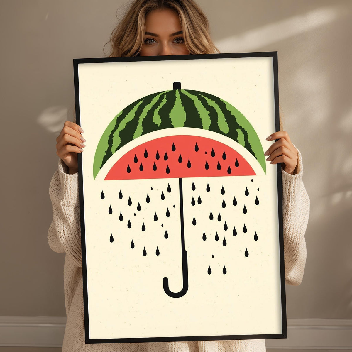 A woman is holding up a framed print with a watermelon design on it, which features a watermelon slice with raindrops falling from it.
