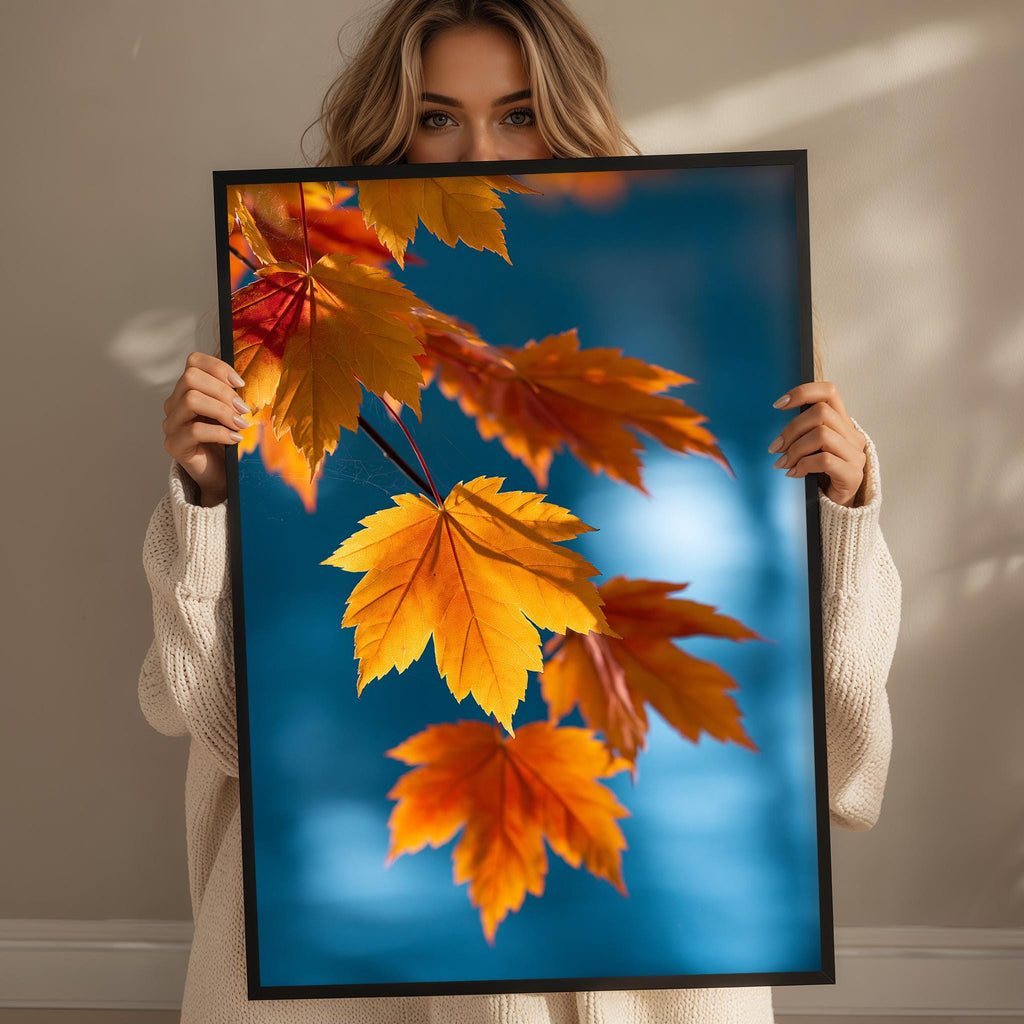 A woman holds up a framed picture of vibrant autumn leaves against a blue background.