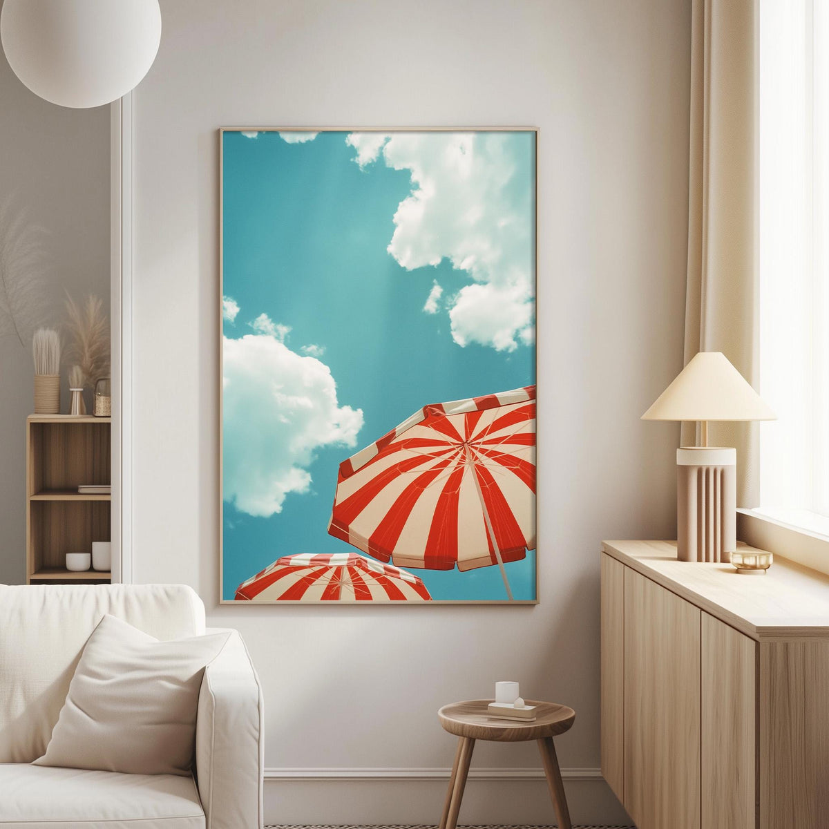 a living room with a large framed picture of two red and white striped umbrellas against a blue sky with white clouds. The picture is hanging on the wall above a white couch.