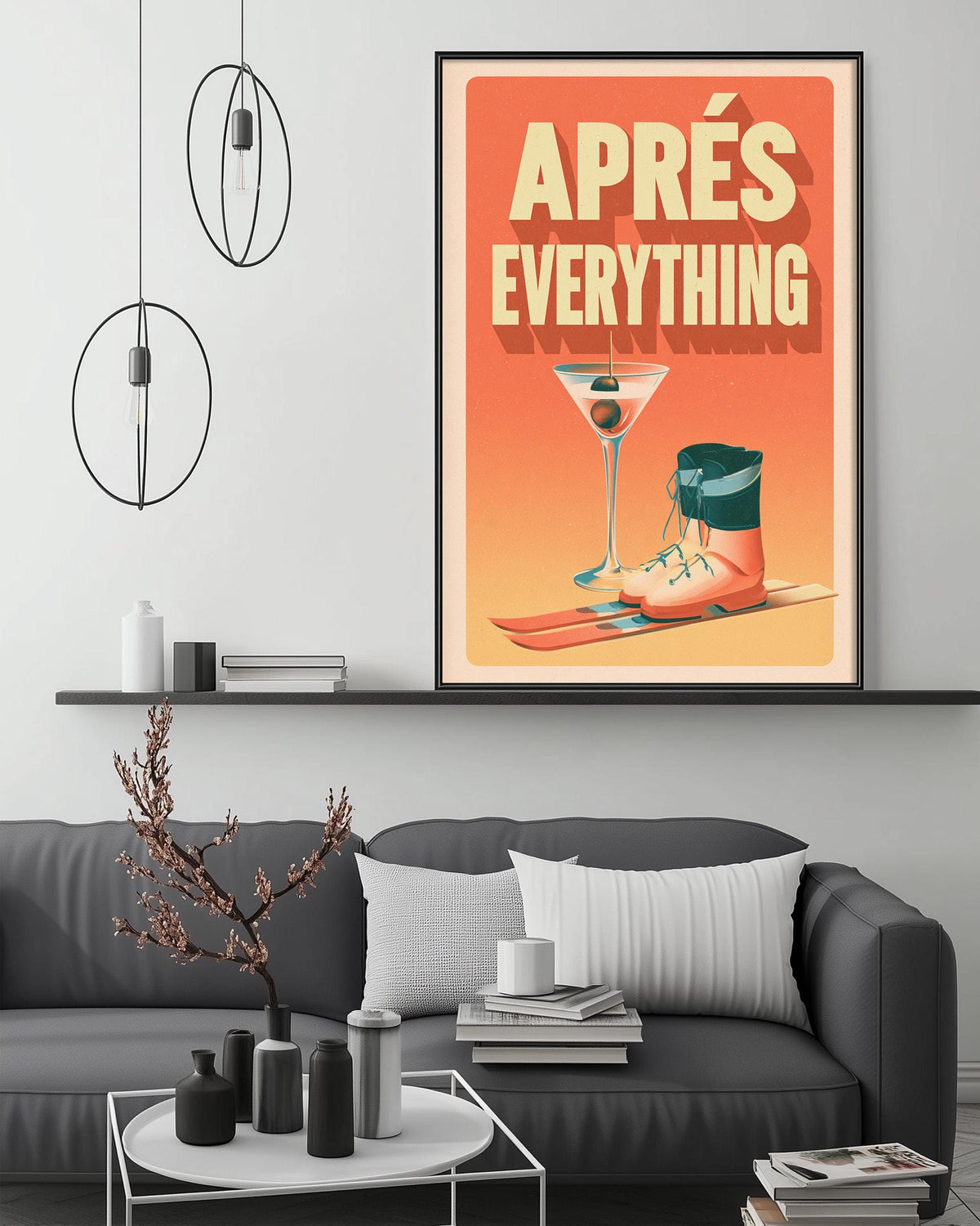 a framed poster with the text "APPRESÉ EVERYTHING" and an illustration of a martini glass and ski boots, hanging on a wall above a gray couch with a coffee table in front of it.