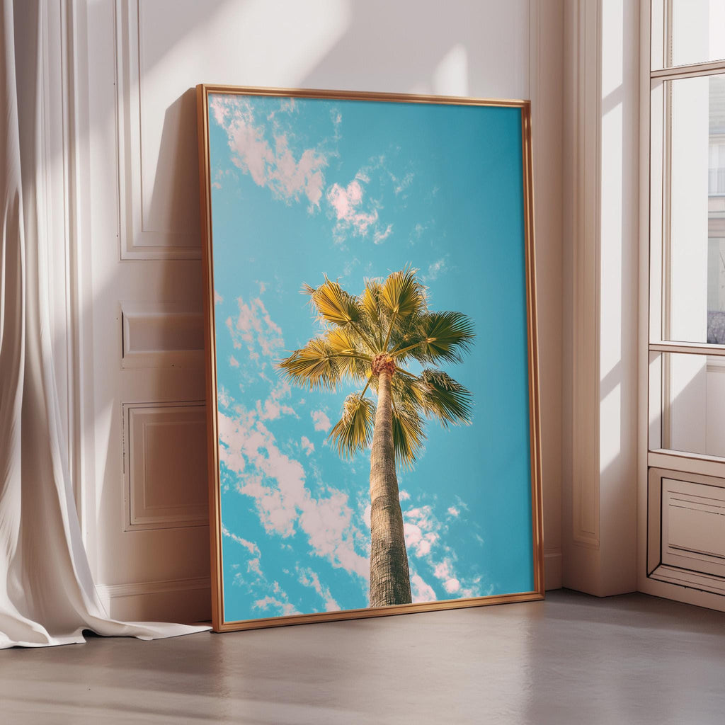 A framed photograph of a palm tree against a bright blue sky with fluffy white clouds.