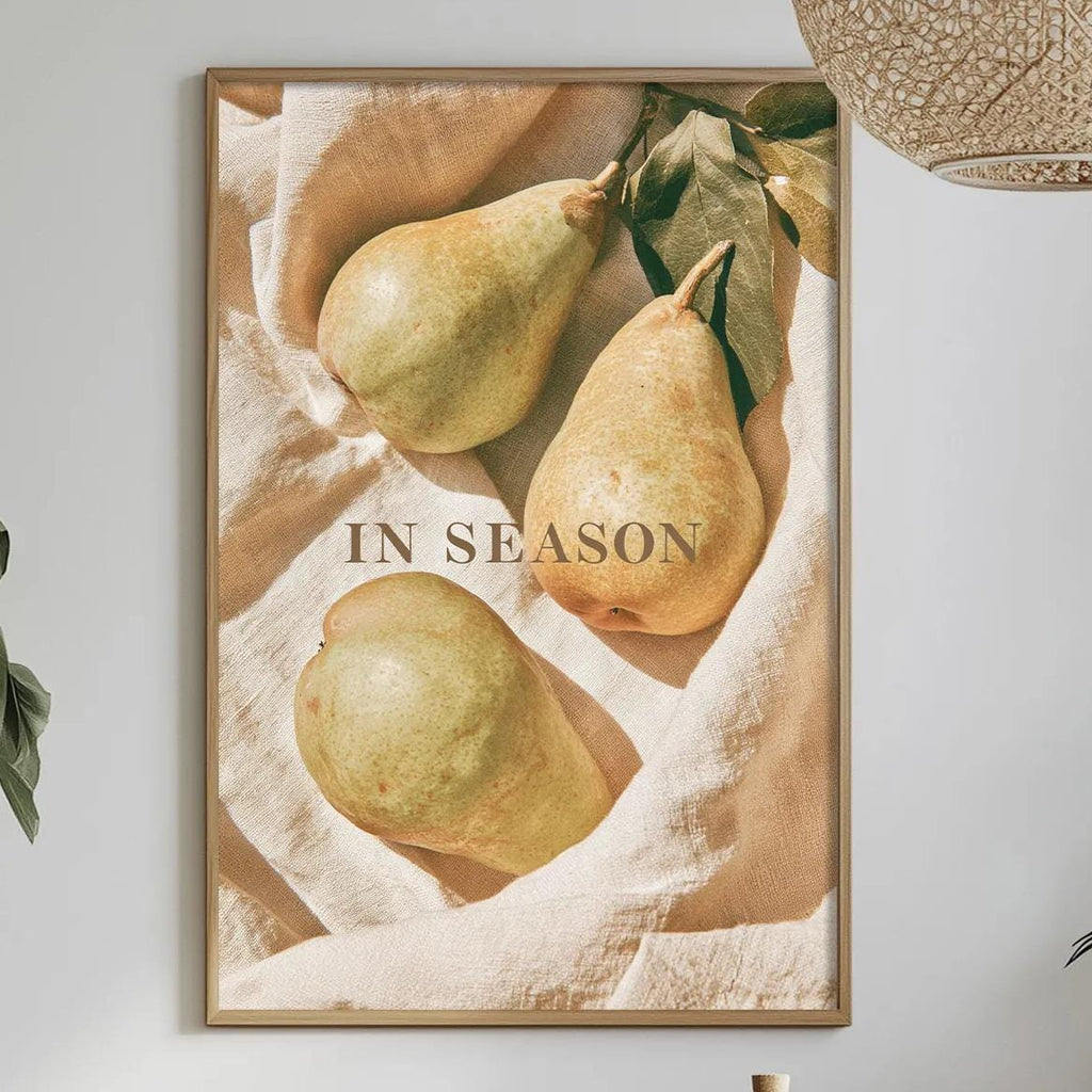 a dining table with a bowl of fruit, a bottle, and a vase of flowers, along with a framed picture of pears hanging on the wall.