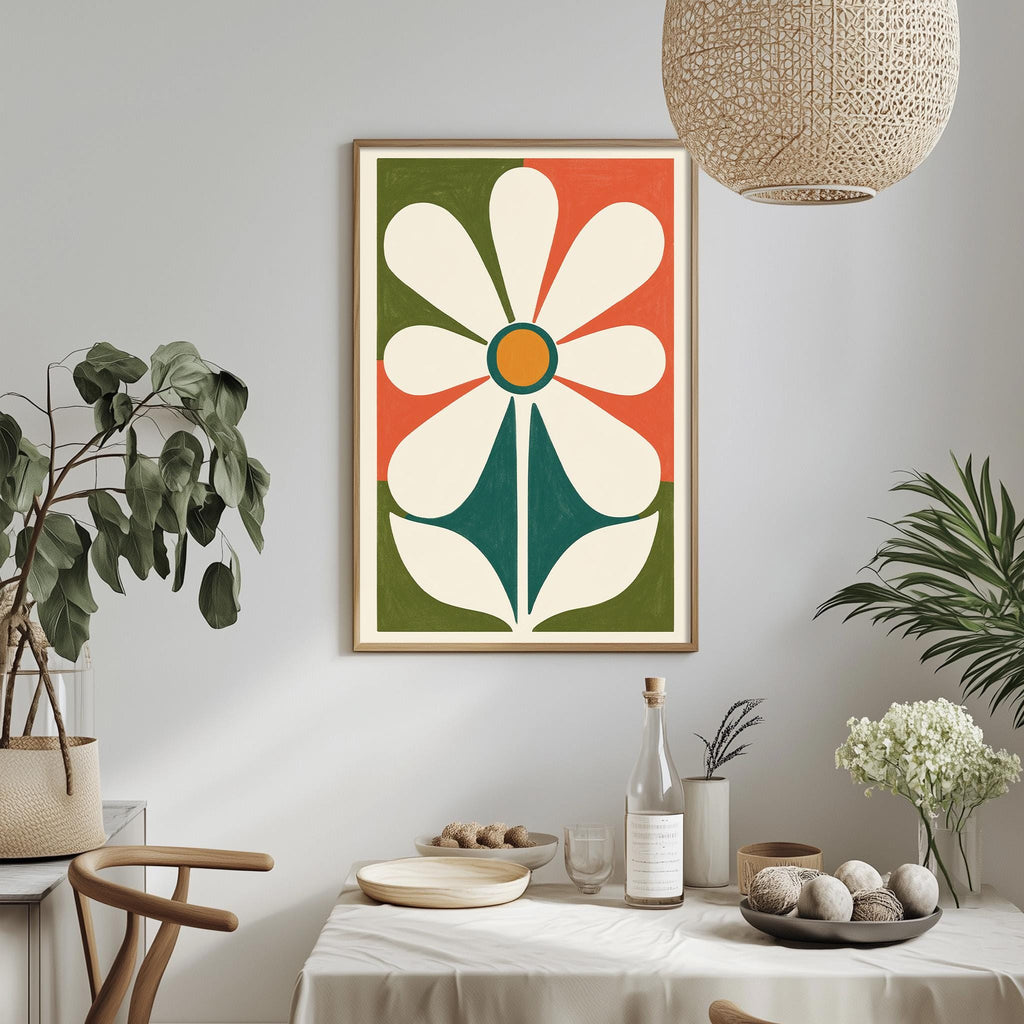 a dining table with a white tablecloth, a bowl of fruit, a bottle, and a vase with flowers. Above the table, there is a framed picture of a flower with a green stem and a white center. The table is set with a plate, a wine glass, and a bottle of wine. The room has a minimalist and modern design, with a woven light fixture hanging above the table and potted plants adding a touch of greenery.