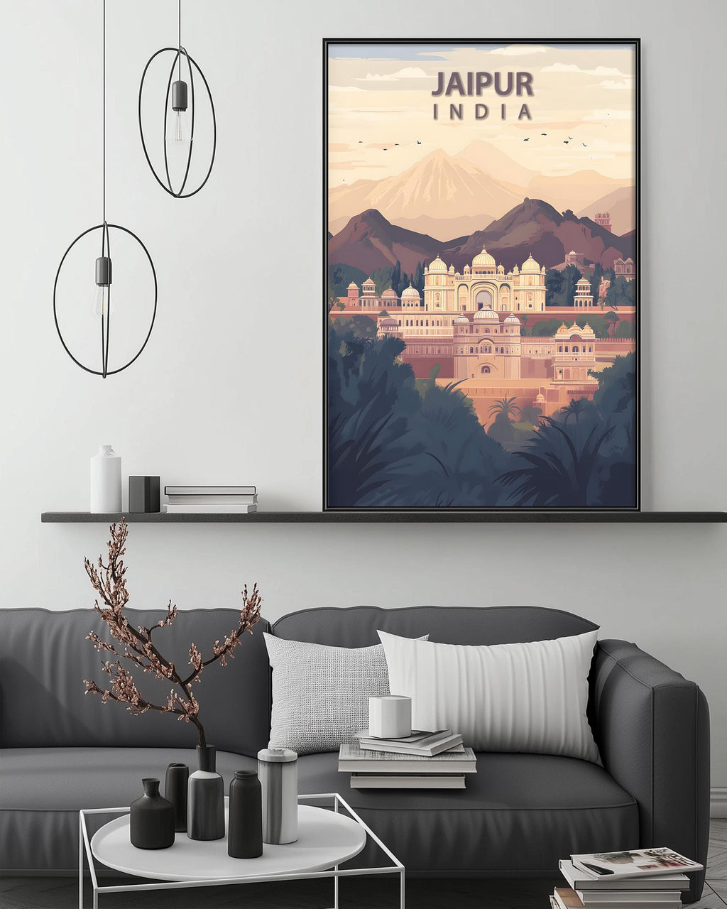 a large framed poster of Jaipur, India, hanging on a wall above a gray couch with a coffee table in front of it. The poster depicts a scenic view of the city, with mountains and buildings in the background. The room has a minimalist and modern design, with a black pendant light hanging above the couch and a shelf displaying decorative items.