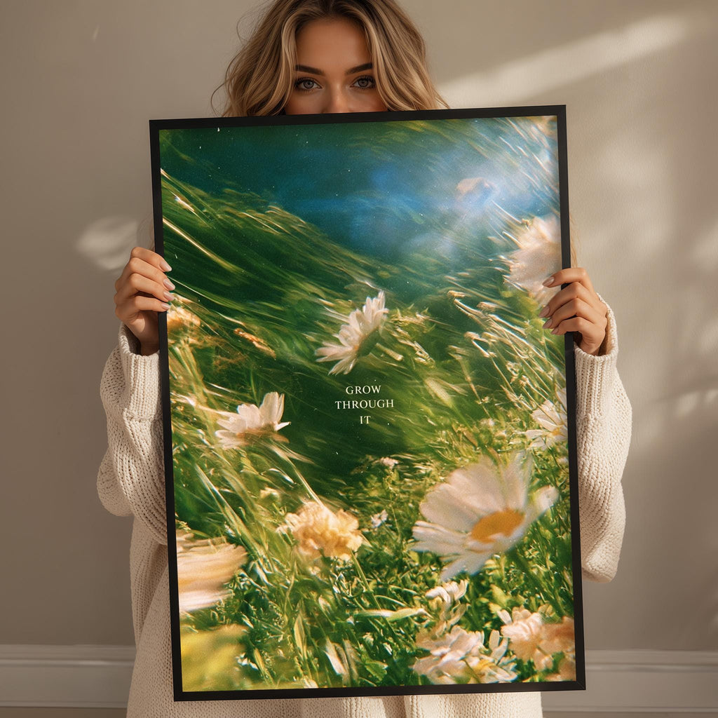 A woman holding a framed poster with a vibrant image of flowers and the text "GROW THROUGH IT" printed on it.