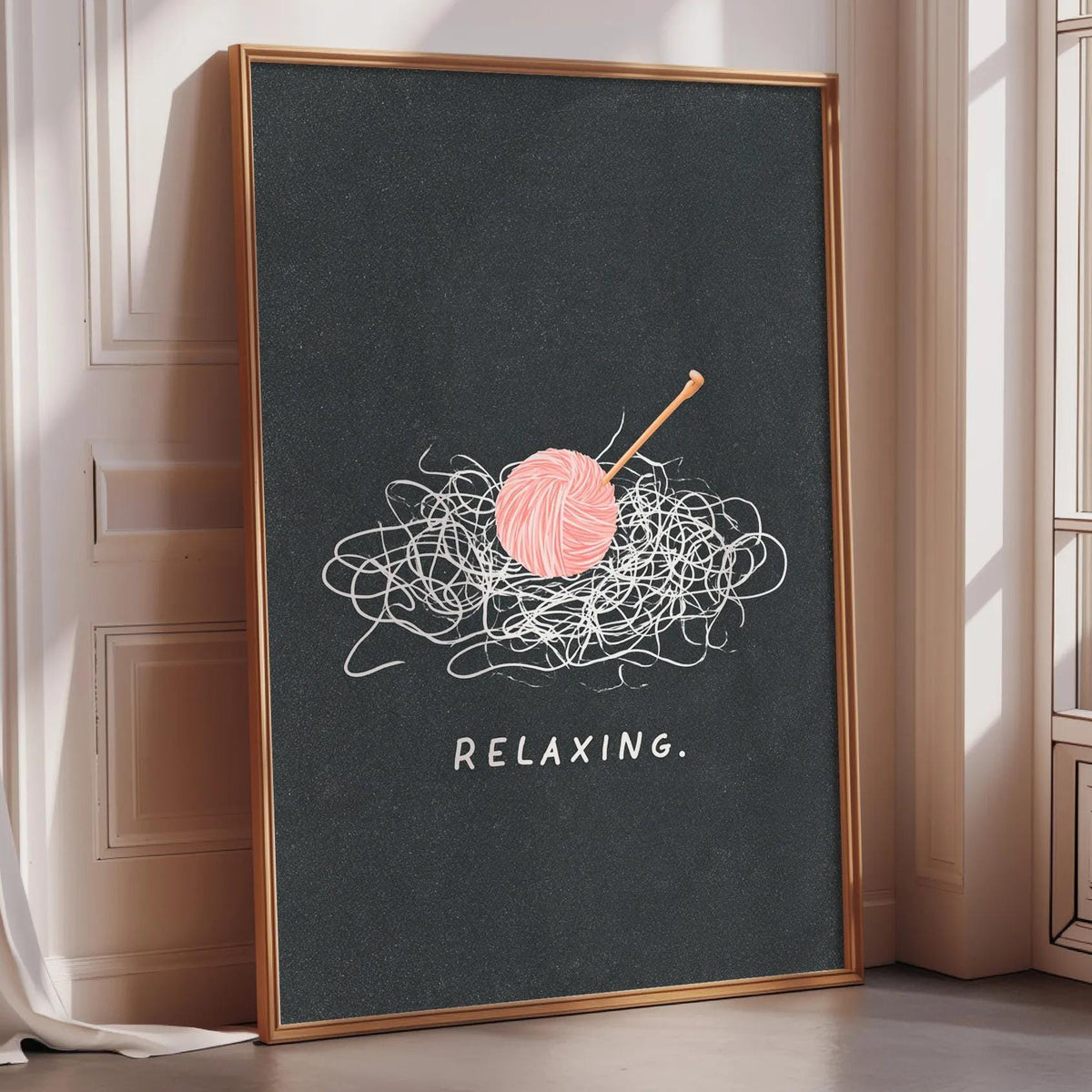 A framed poster with a black background and a pink ball of yarn with a crochet hook on top, along with the text "RELAXING."
