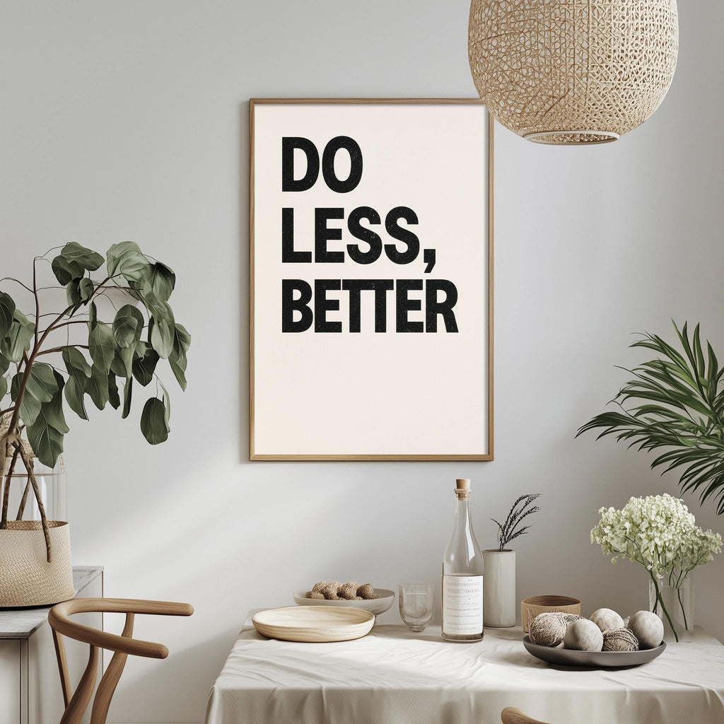 a framed poster with the text "DO LESS, BETTER" hanging on a wall above a dining table with various items on it, including a bottle, a bowl, and some plants.