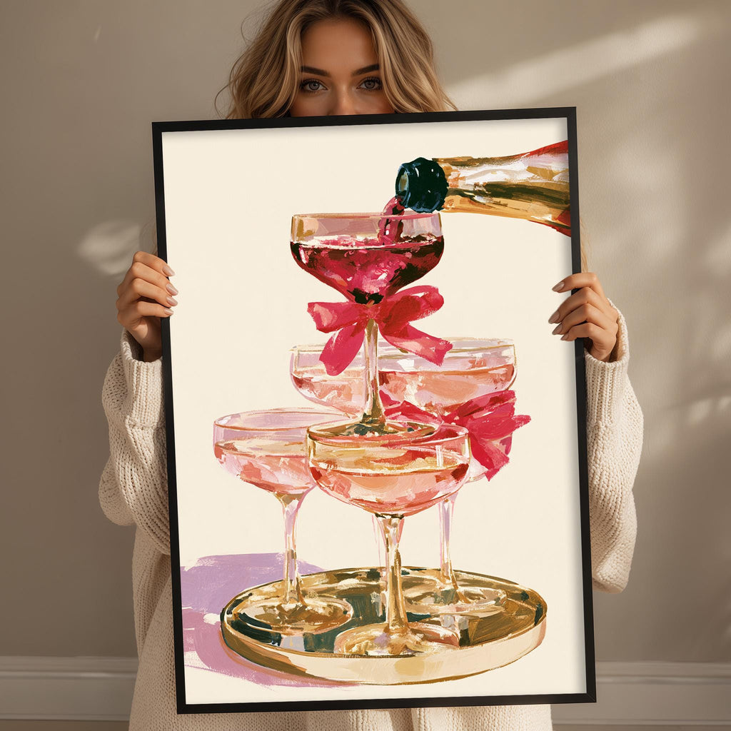 A woman holds up a framed picture of pink champagne glasses with a champagne bottle being poured into them.