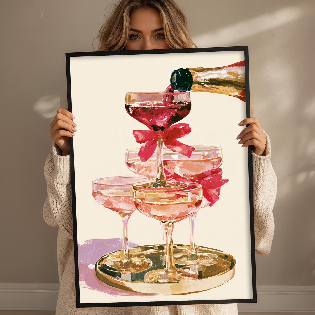 A woman holds up a framed picture of pink champagne glasses with a champagne bottle being poured into them.