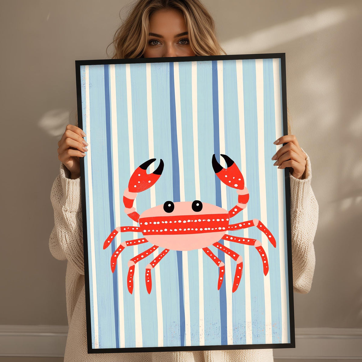 A woman is holding up a framed picture of a red crab against a blue striped background.