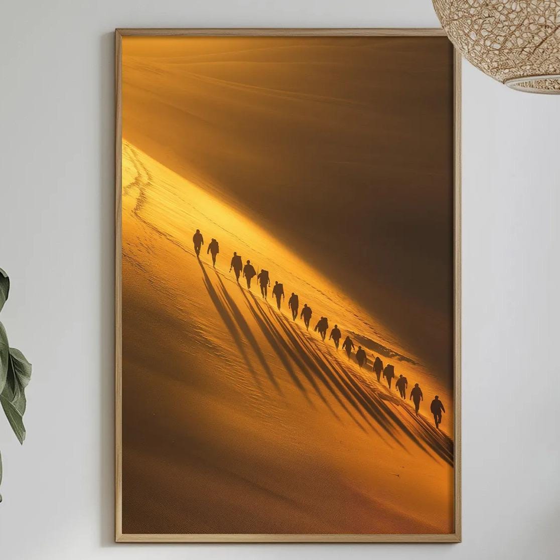 a dining table with a white tablecloth, a bowl of fruit, a bottle, and a vase with flowers. Above the table, there is a framed picture of a group of people walking in a line, with a warm, golden-orange background.