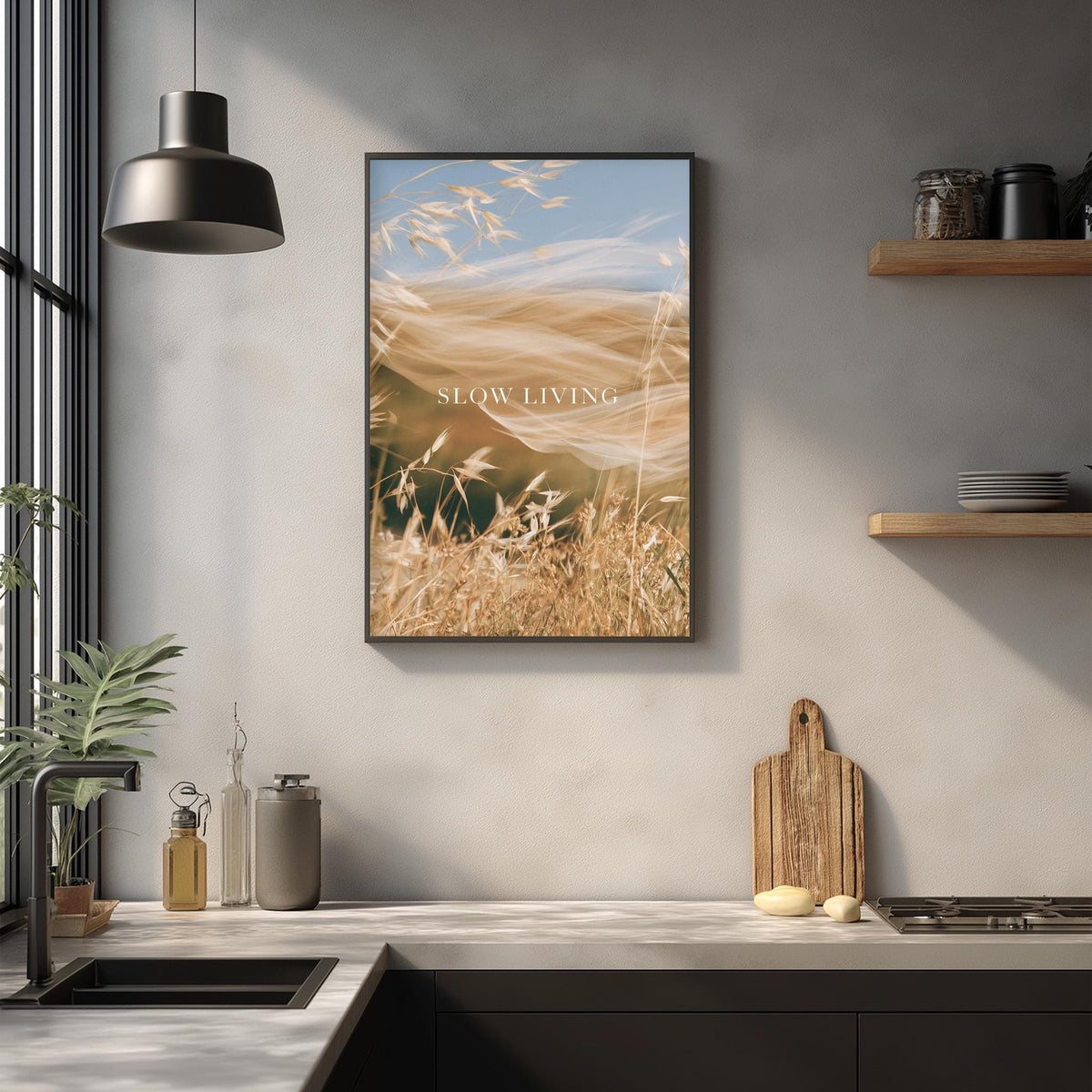 a kitchen counter with a framed picture of a field of tall grass, a wooden cutting board, and various kitchen items such as a bottle, a cup, and a bowl.