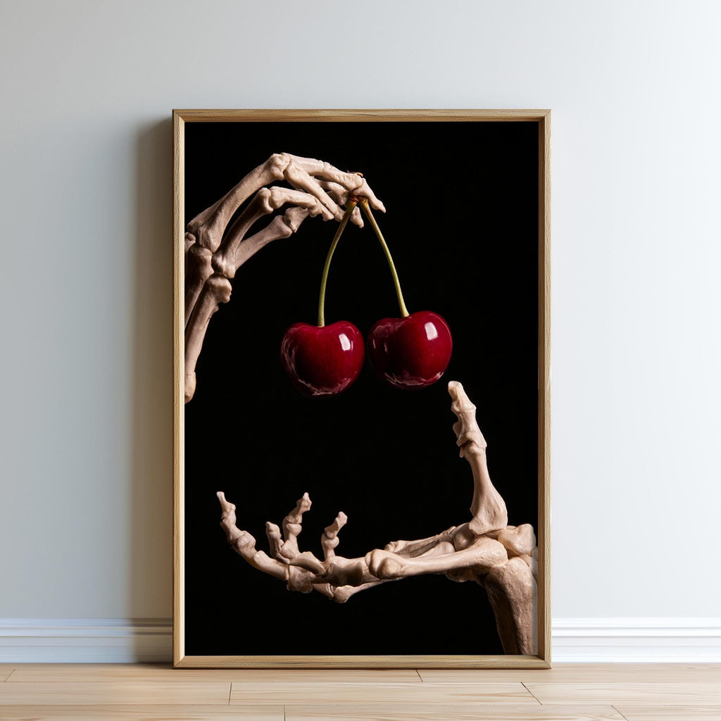 A framed image of a skeletal hand holding two red cherries against a black background.