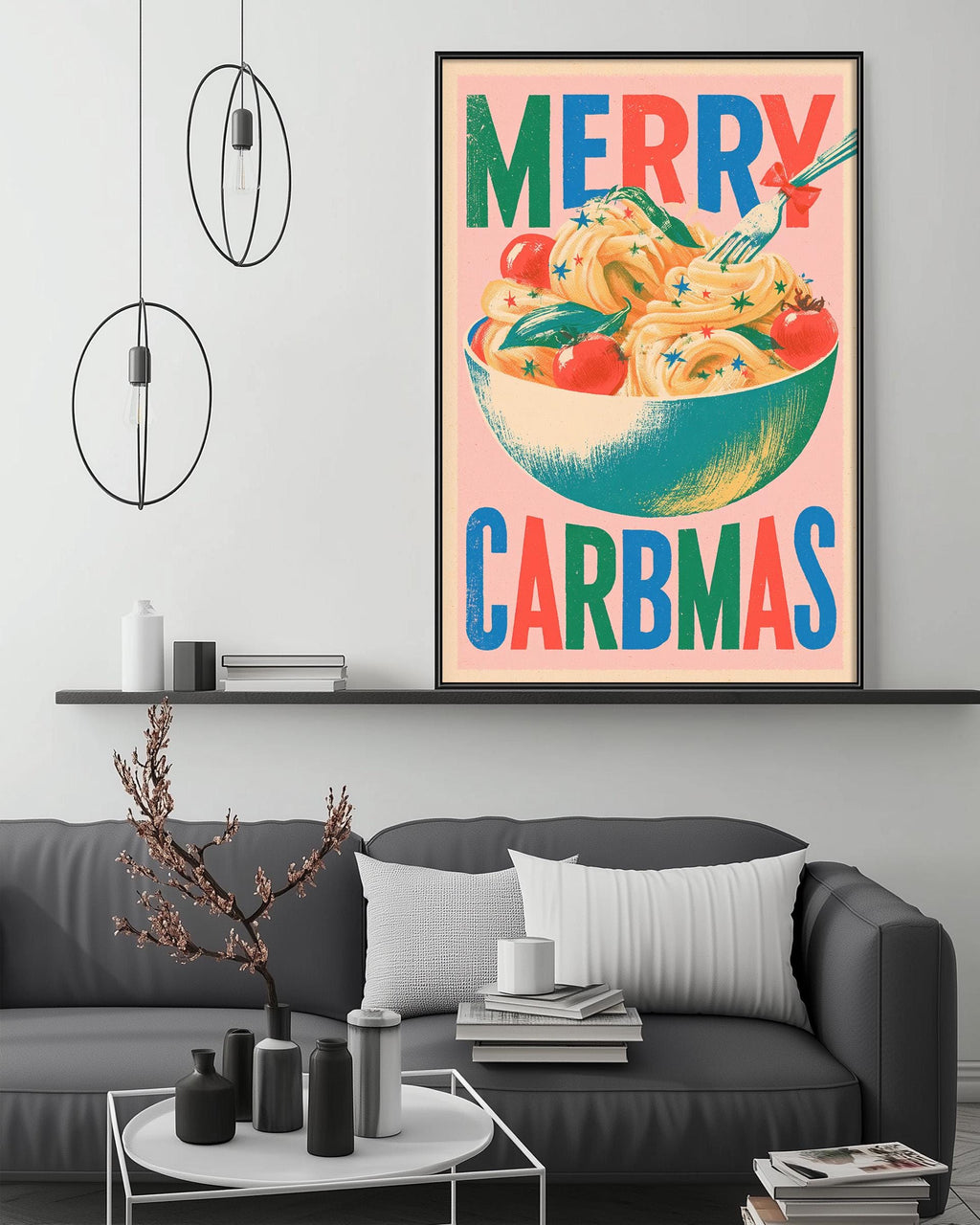 a large framed poster with a colorful illustration of a bowl of food, along with the text "MERRY CARBMAS" displayed prominently. The poster is hanging on a wall above a gray couch, which has a coffee table in front of it. The room also contains various decorative items, such as a potted plant, vases, and books, creating a cozy and inviting atmosphere.