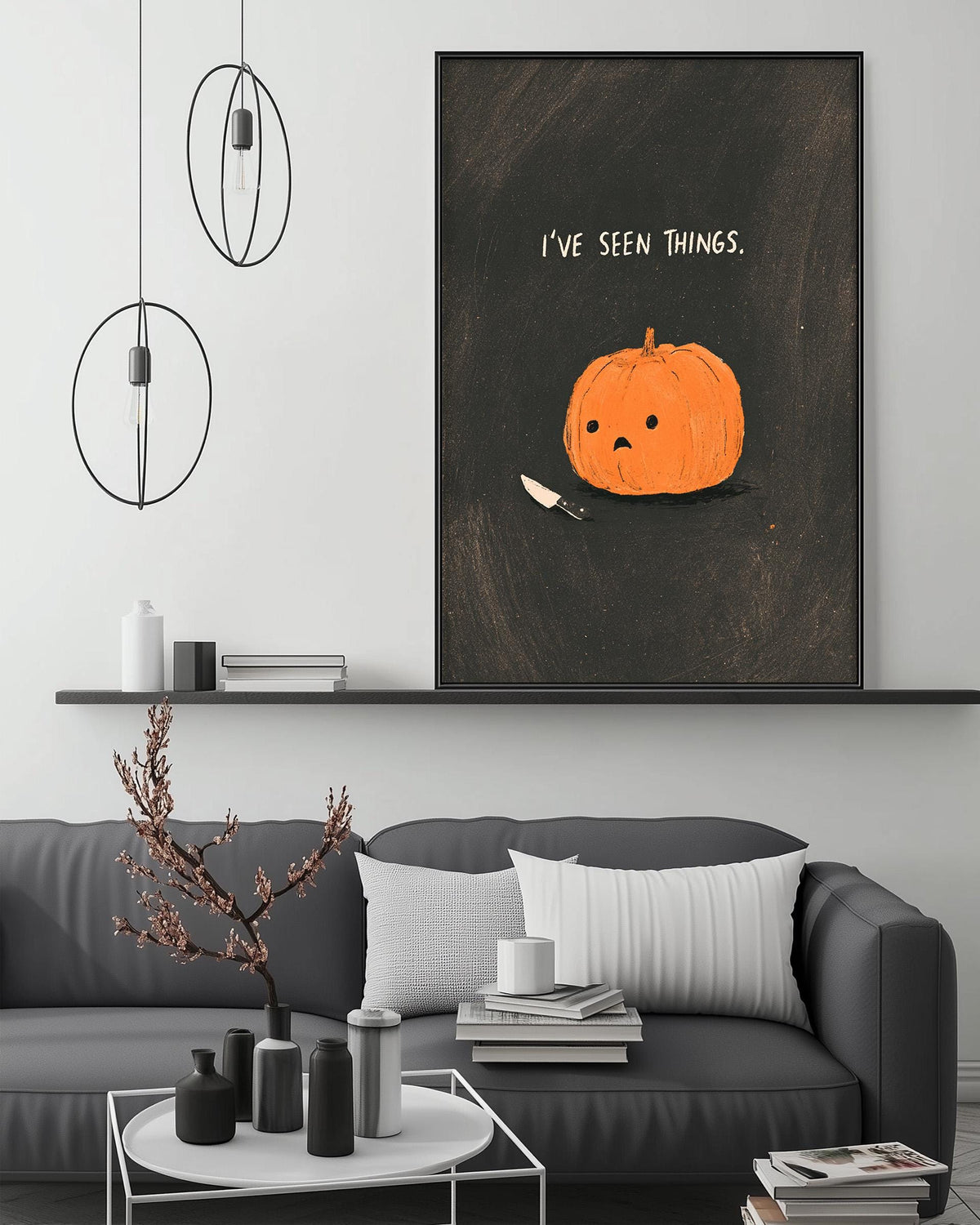a cozy living room with a gray sofa, a coffee table, and a large framed poster of a pumpkin with a face on it. The poster has the text "I've seen things" written on it.