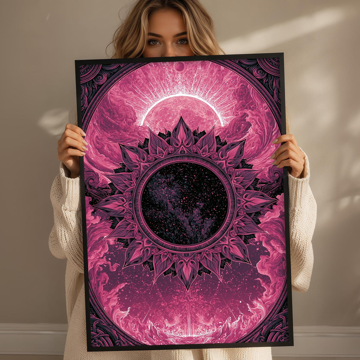 A woman holds up a framed poster with a vibrant, abstract design featuring a sun, moon, and floral patterns in shades of pink and purple.