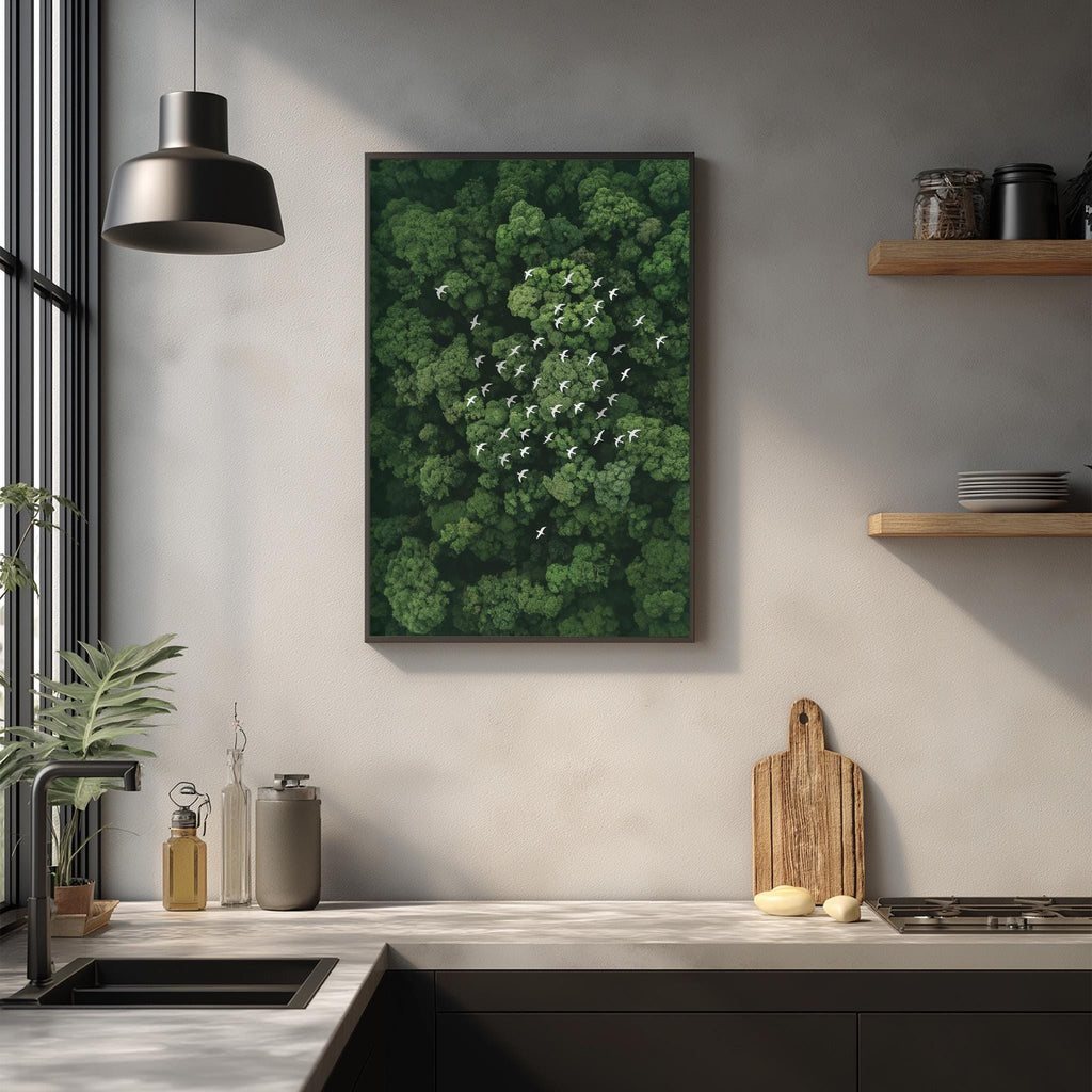 a kitchen counter with various kitchen items, including a cutting board, a sink, and a potted plant. Above the counter, there is a framed picture of a lush green forest with a flock of birds in the sky.