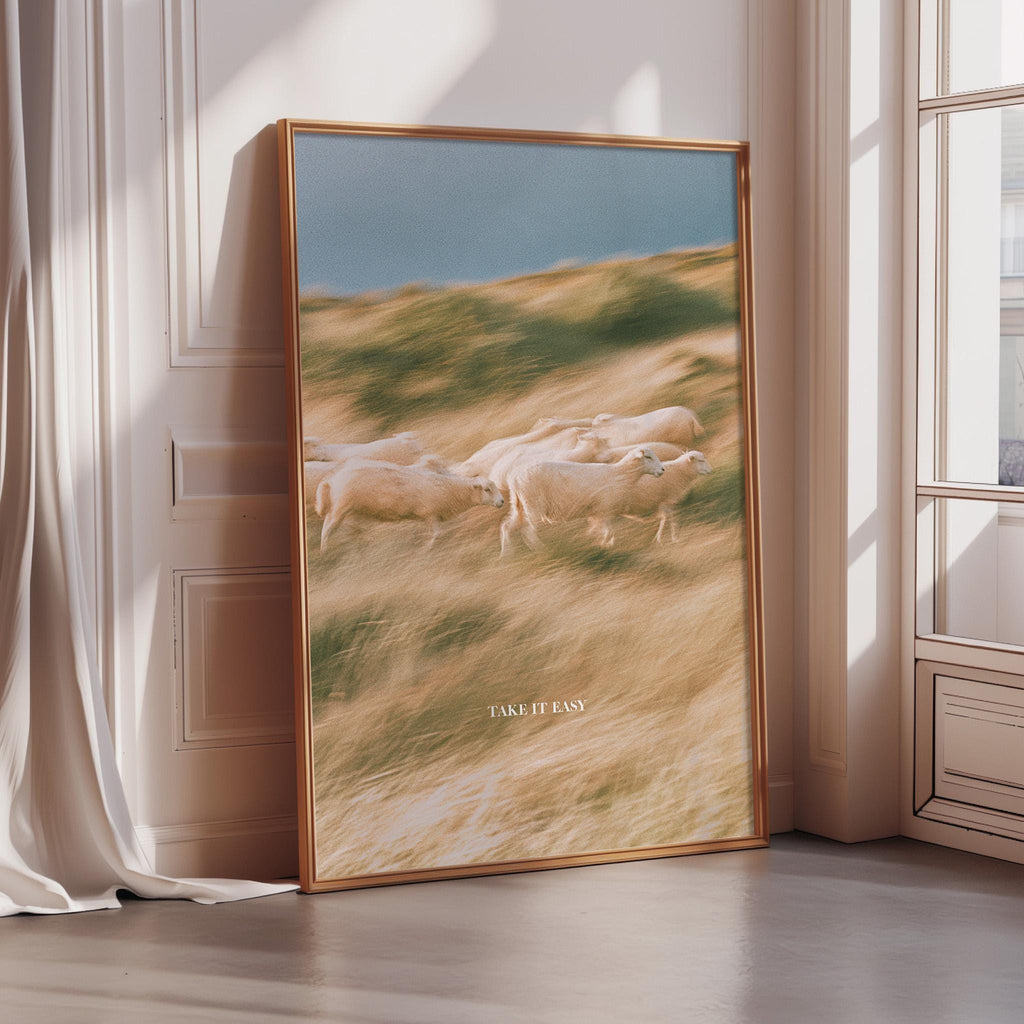 A large framed picture depicting a group of sheep running through a grassy field, with the text "TAKE IT EASY" written on the bottom of the frame.