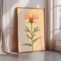 A framed illustration of a vibrant orange flower with green leaves is displayed on a wall in a room with sunlight streaming in from a window.