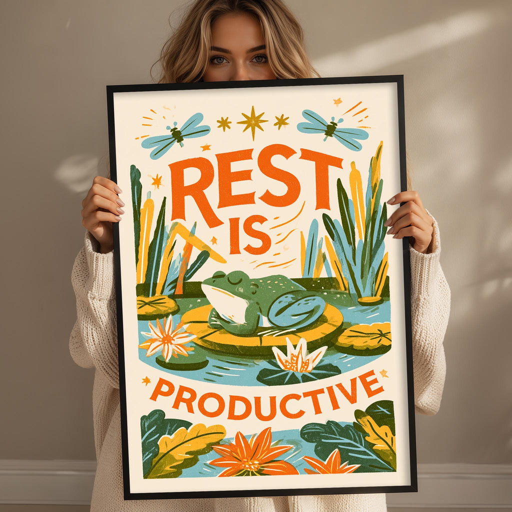 A woman is holding up a framed poster with a frog and water lilies, along with the text "REST IS PRODUCTIVE".