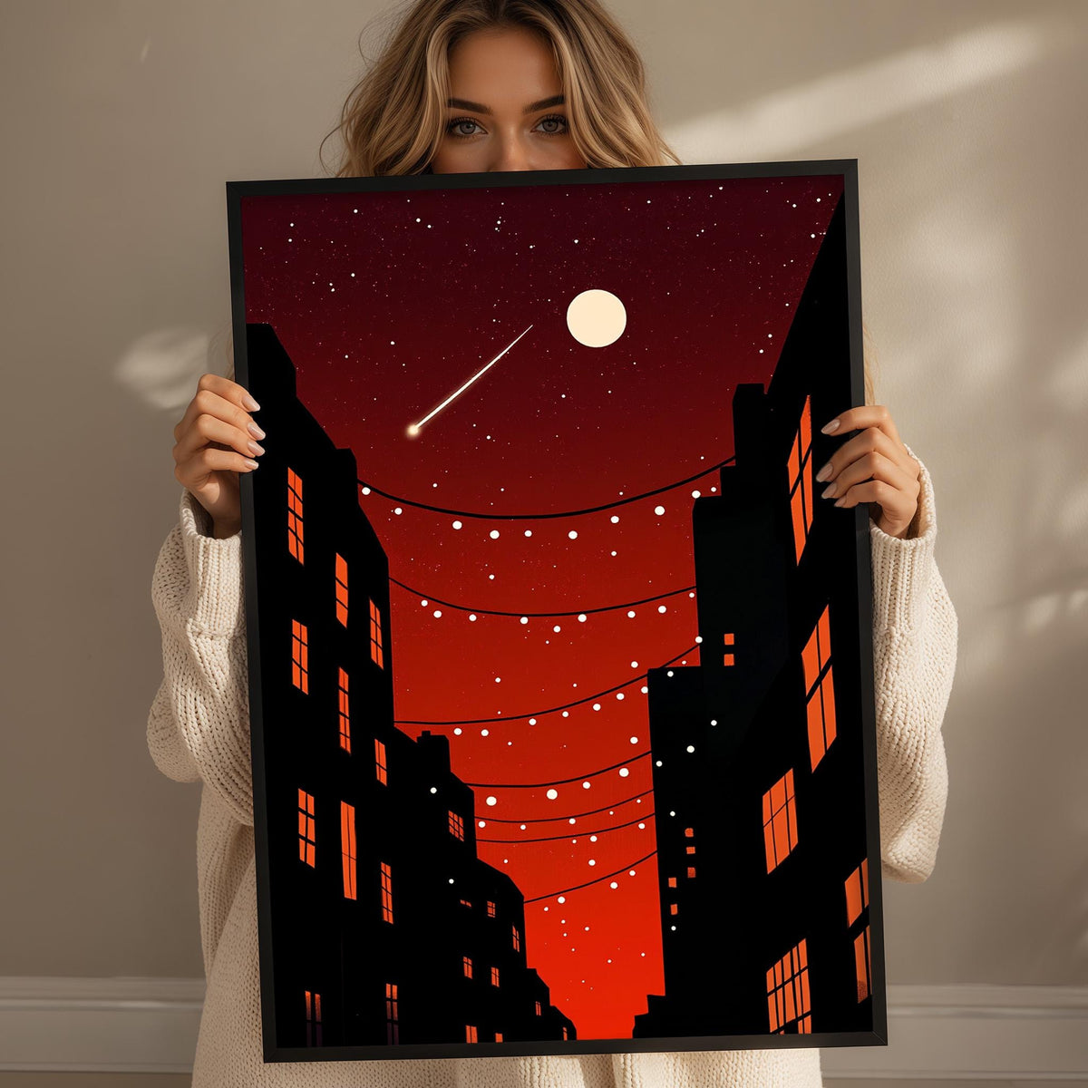 A woman holds up a framed poster depicting a nighttime cityscape with a full moon, stars, and a string of lights.
