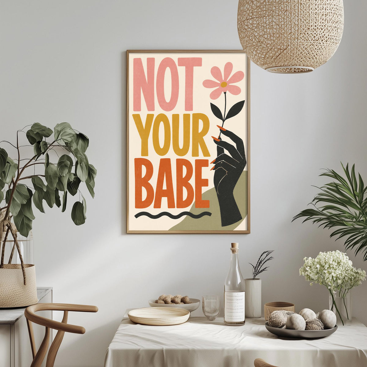 a framed poster with the text "NOT YOUR BABE" hanging on a wall above a dining table with various items on it.