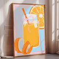 A framed illustration of a glass of orange juice with a slice of orange on the side, set against a light blue background.