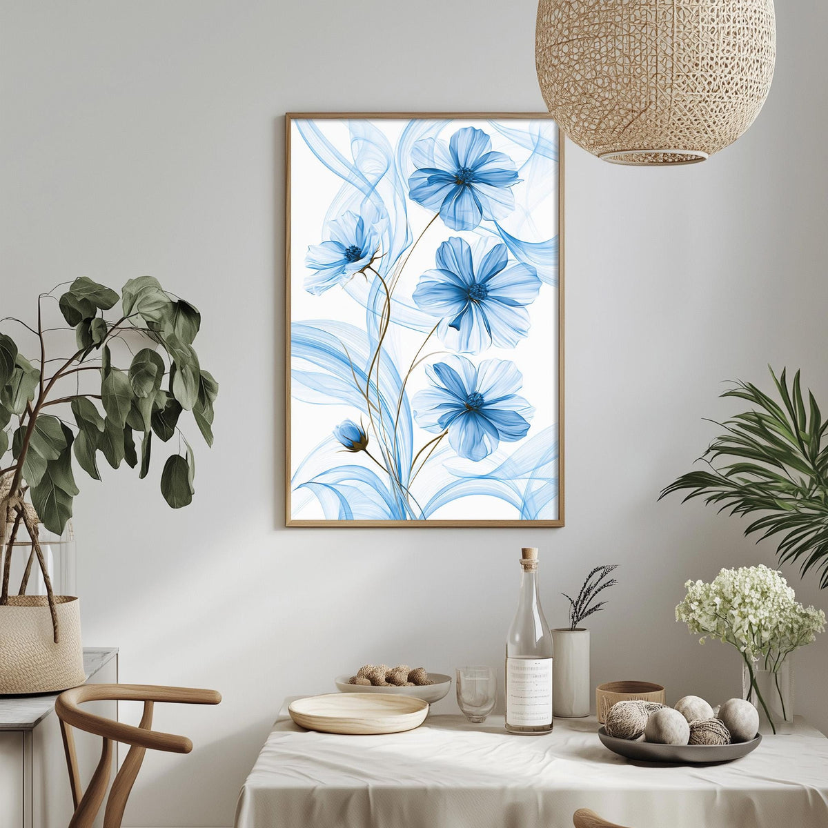 a dining table with a white tablecloth, a bowl of fruit, a bottle, and a vase with flowers. Above the table, there is a framed picture of blue flowers hanging on the wall.