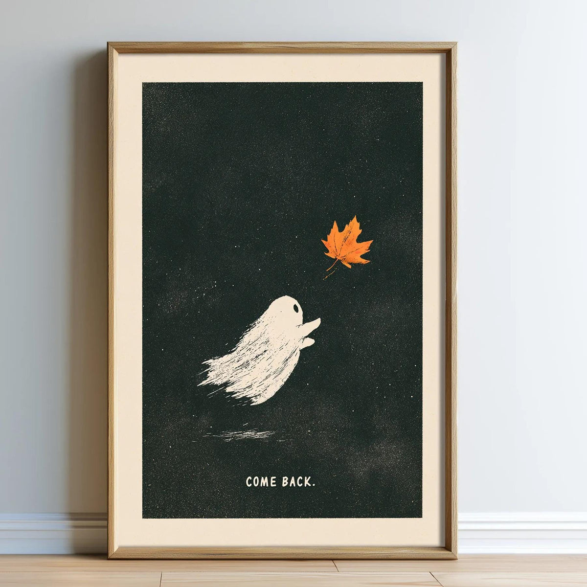 The image is a framed artwork depicting a ghost floating in the air with a single orange leaf attached to its hand, against a dark background.