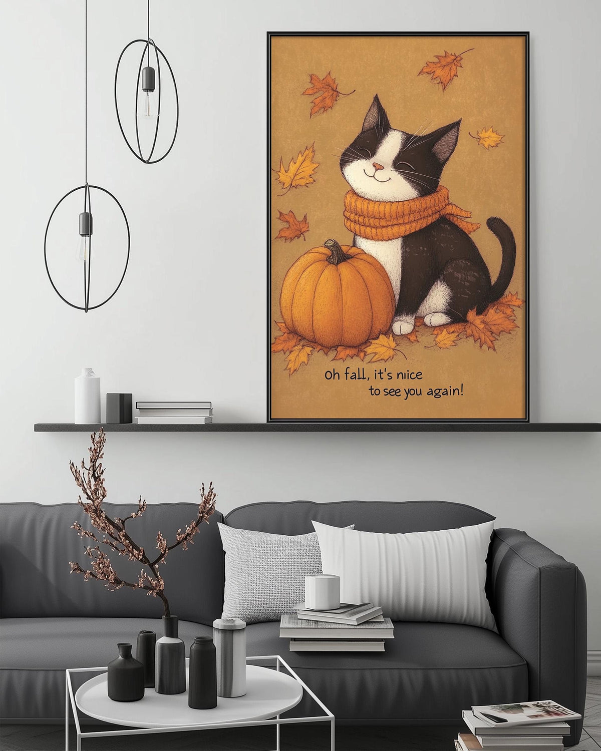 a cozy living room with a gray couch, a coffee table, and a framed illustration of a cat sitting next to a pumpkin. The cat is wearing a scarf and appears to be enjoying the fall season. The room has a minimalist and modern design, with a white wall and a shelf displaying decorative items.