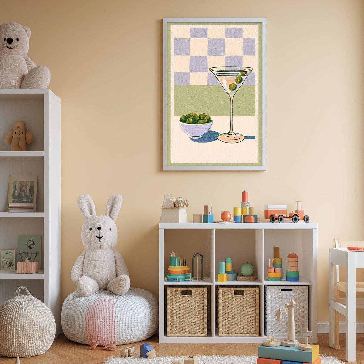 A cozy children's room with a white bookshelf, a plush rabbit, and a colorful toy box filled with toys. A framed illustration of a martini glass with olives is displayed on the wall above the toy box.