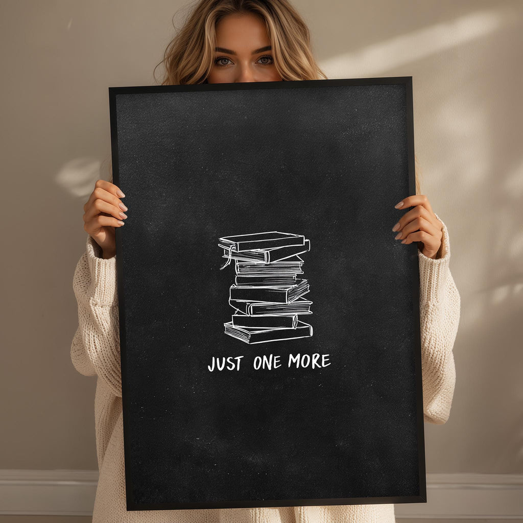 A woman holding a black poster with a stack of books and the text "JUST ONE MORE" written on it.