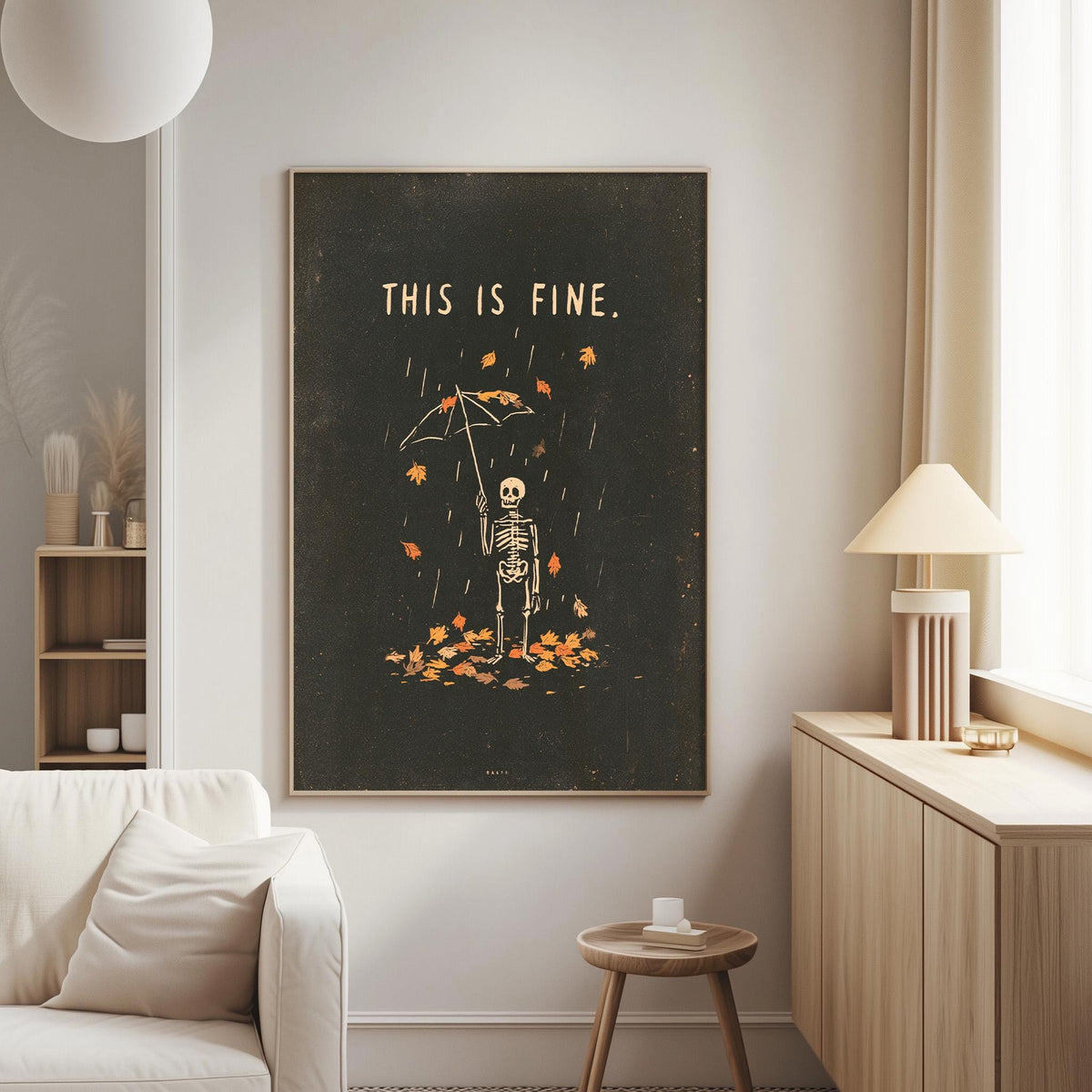 a living room with a large black framed poster on the wall that says "THIS IS FINE." The poster depicts a skeleton holding an umbrella, surrounded by falling leaves. The room also includes a white couch, a small table, and a lamp.