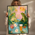 A woman holds up a framed painting depicting two green frogs sitting at a table with a glass of wine and playing cards.