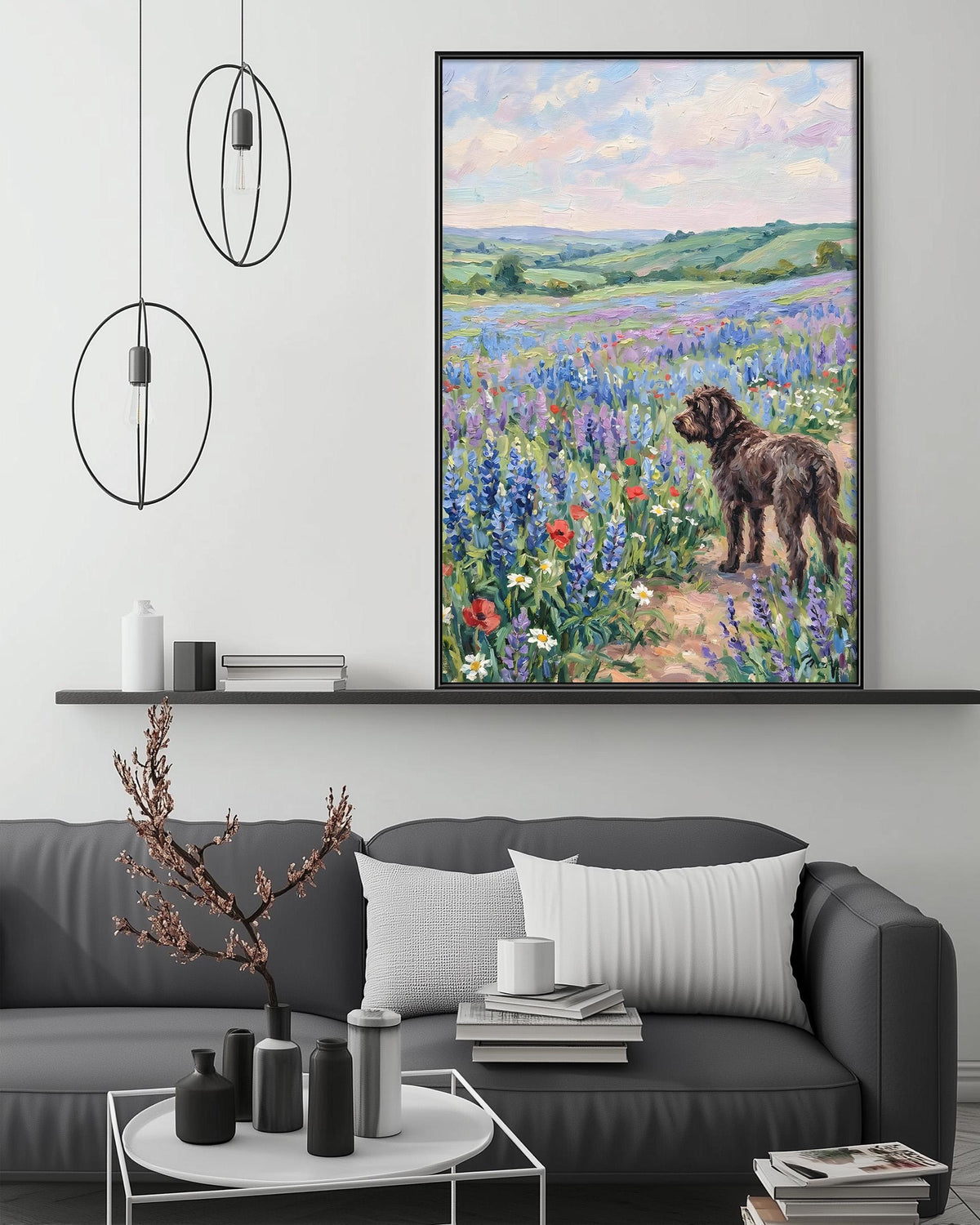 a large painting of a dog standing in a field of flowers, with a serene landscape in the background. The painting is hung on a wall above a gray couch, which has a coffee table in front of it. The room also includes a shelf with decorative items and a potted plant.