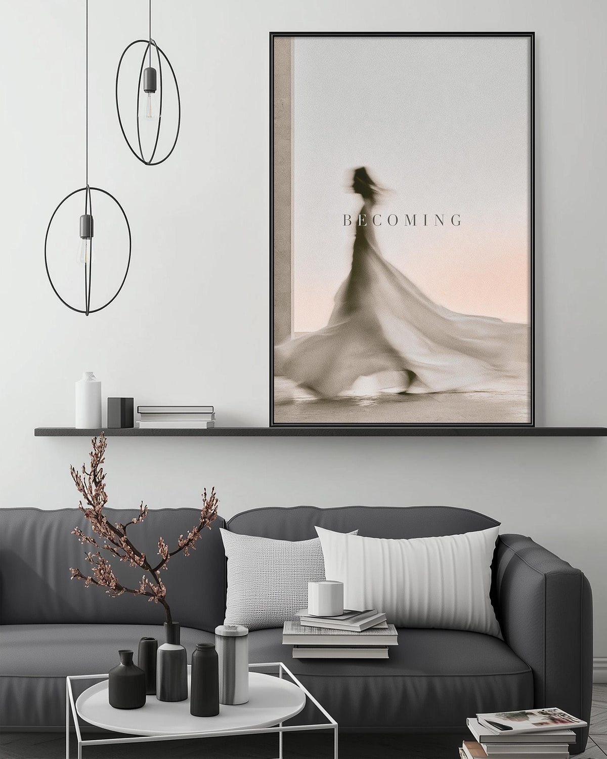 a modern living room with a gray sofa, a coffee table, and a large framed artwork depicting a woman in a flowing dress. The artwork is hanging above the sofa, and the room has a minimalist and stylish design with pendant lights, a shelf, and decorative elements such as a vase and a book.