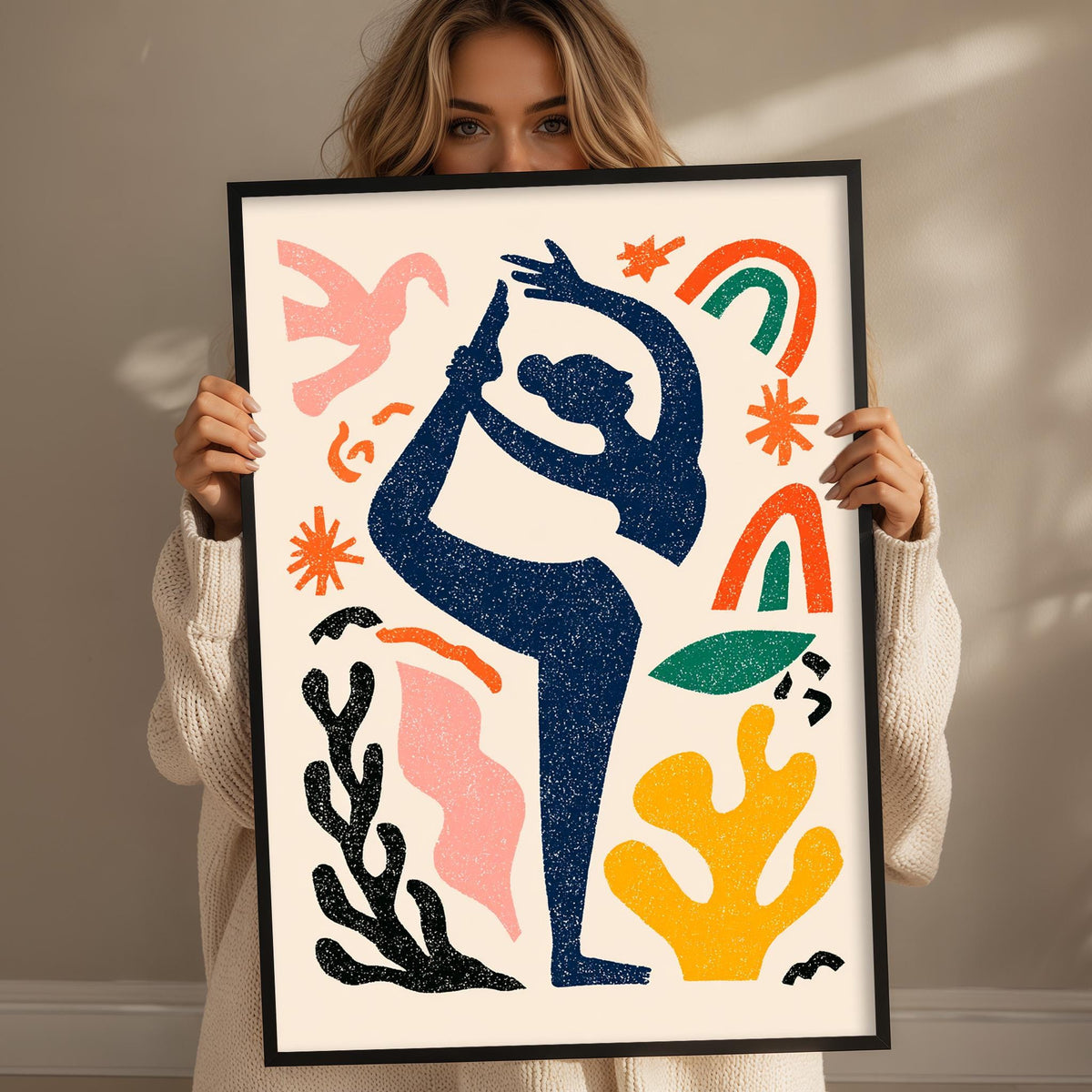 A woman is holding up a framed artwork featuring a stylized figure in a yoga pose, surrounded by various abstract shapes and designs.