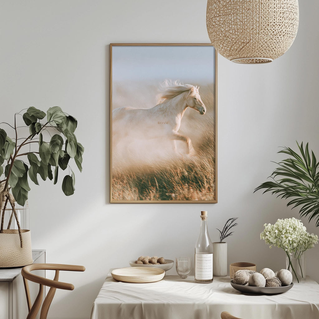 a dining table with a white tablecloth, a bowl of fruit, a bottle, and a vase with flowers. Above the table, there is a framed picture of a horse running in a field.