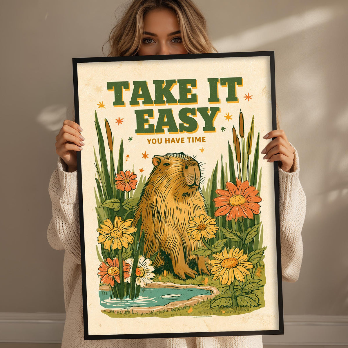A woman holding a framed poster with an illustration of a beaver surrounded by flowers and plants.