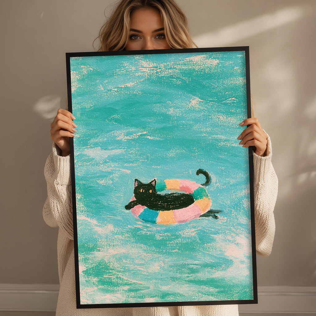 A woman holds up a framed painting depicting a black cat swimming in a colorful inner tube in a turquoise ocean.
