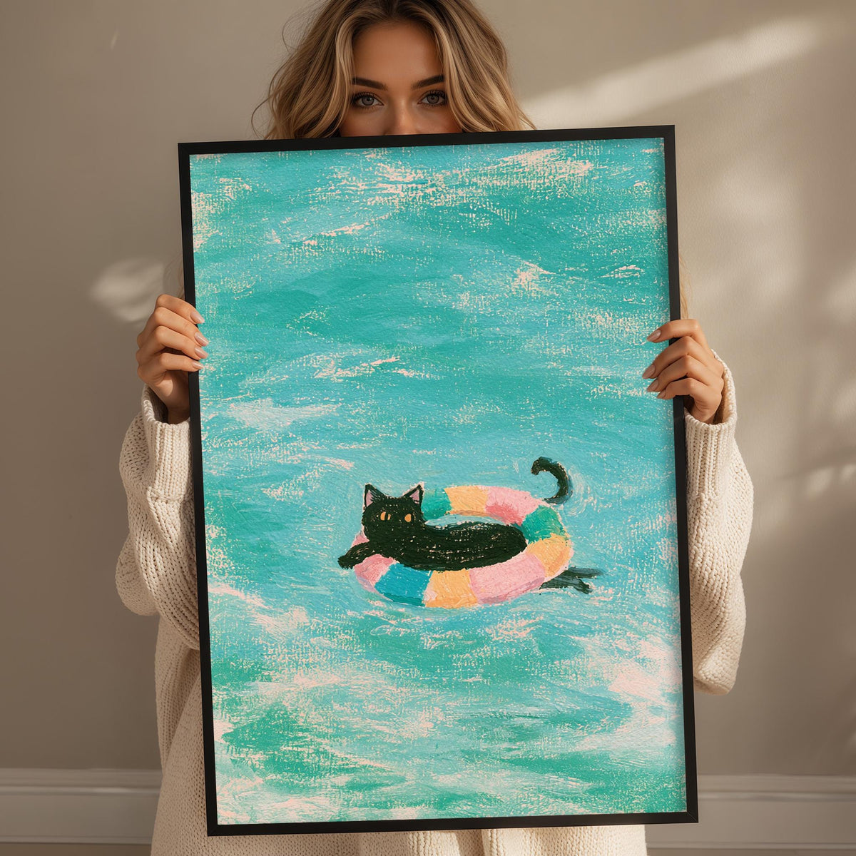A woman holds up a framed painting depicting a black cat swimming in a colorful inner tube in a turquoise ocean.