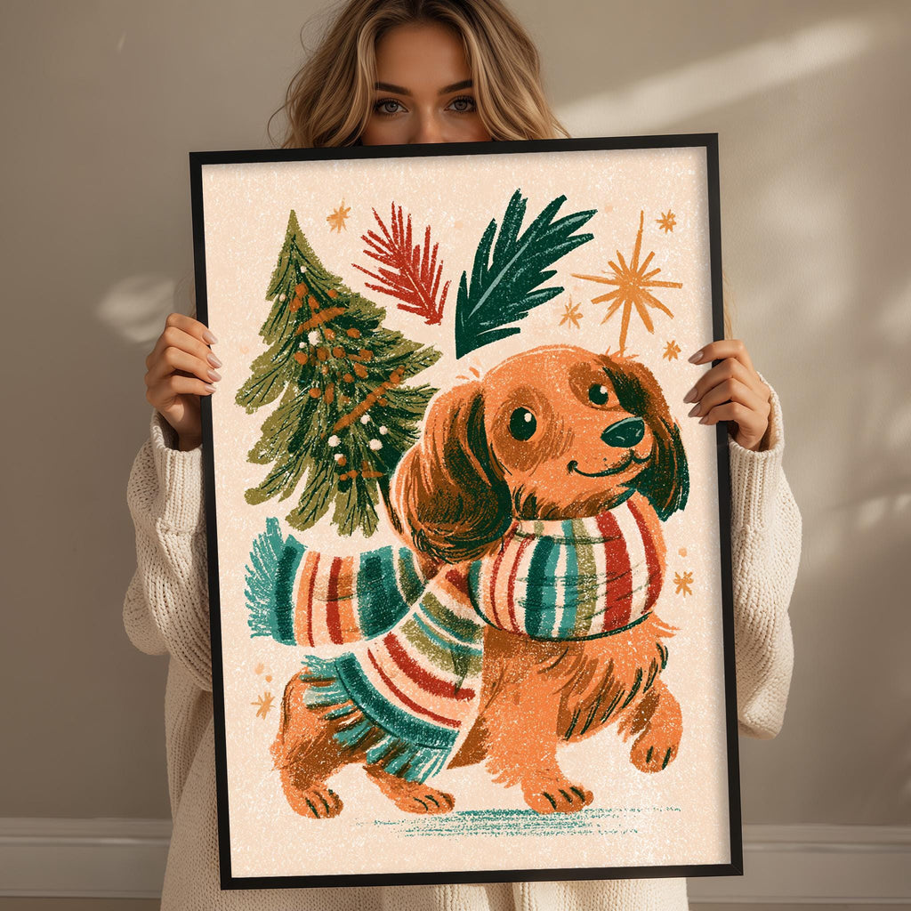 A woman is holding up a framed illustration of a dog wearing a colorful scarf and surrounded by festive holiday elements such as a Christmas tree and stars.