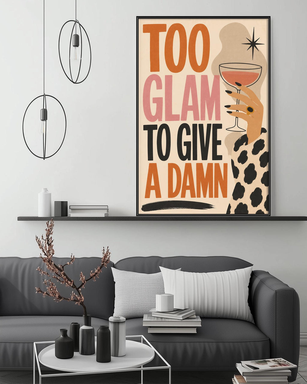 a modern living room with a gray sofa, a coffee table, and a framed poster on the wall. The poster has a bold text that reads "Too Glam to Give a Damn" and includes an illustration of a hand holding a wine glass.