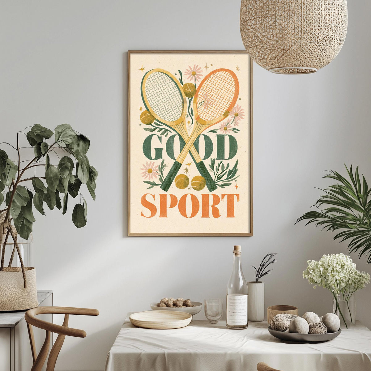 a framed poster with the text "GOOD SPORT" hanging on a wall above a dining table with various items on it, including a bottle, a bowl, and a vase.