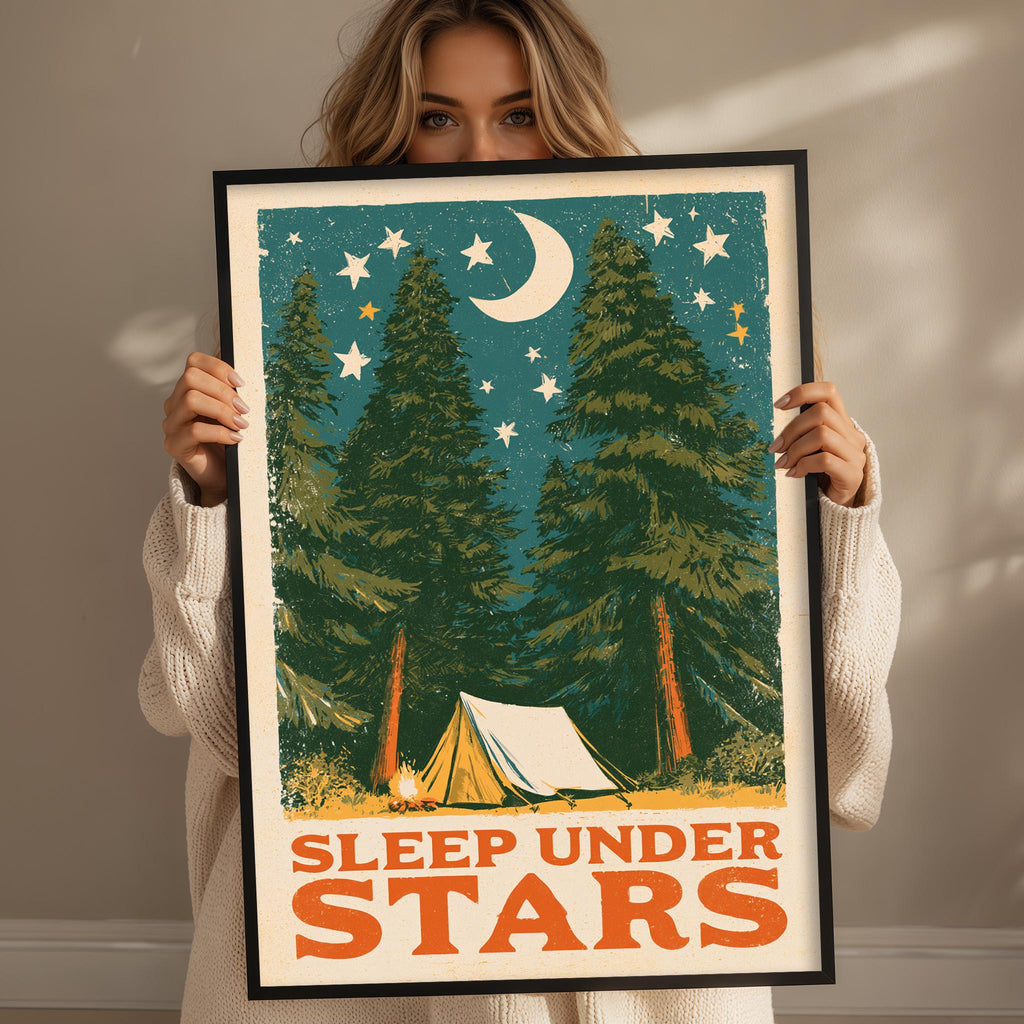 A woman holding a framed poster with a nighttime scene of pine trees, a crescent moon, and stars.