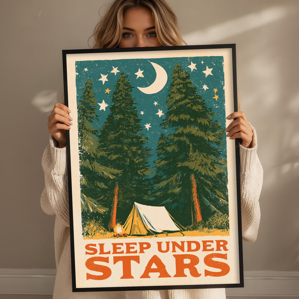 A woman holding a framed poster with a nighttime scene of pine trees, a crescent moon, and stars.