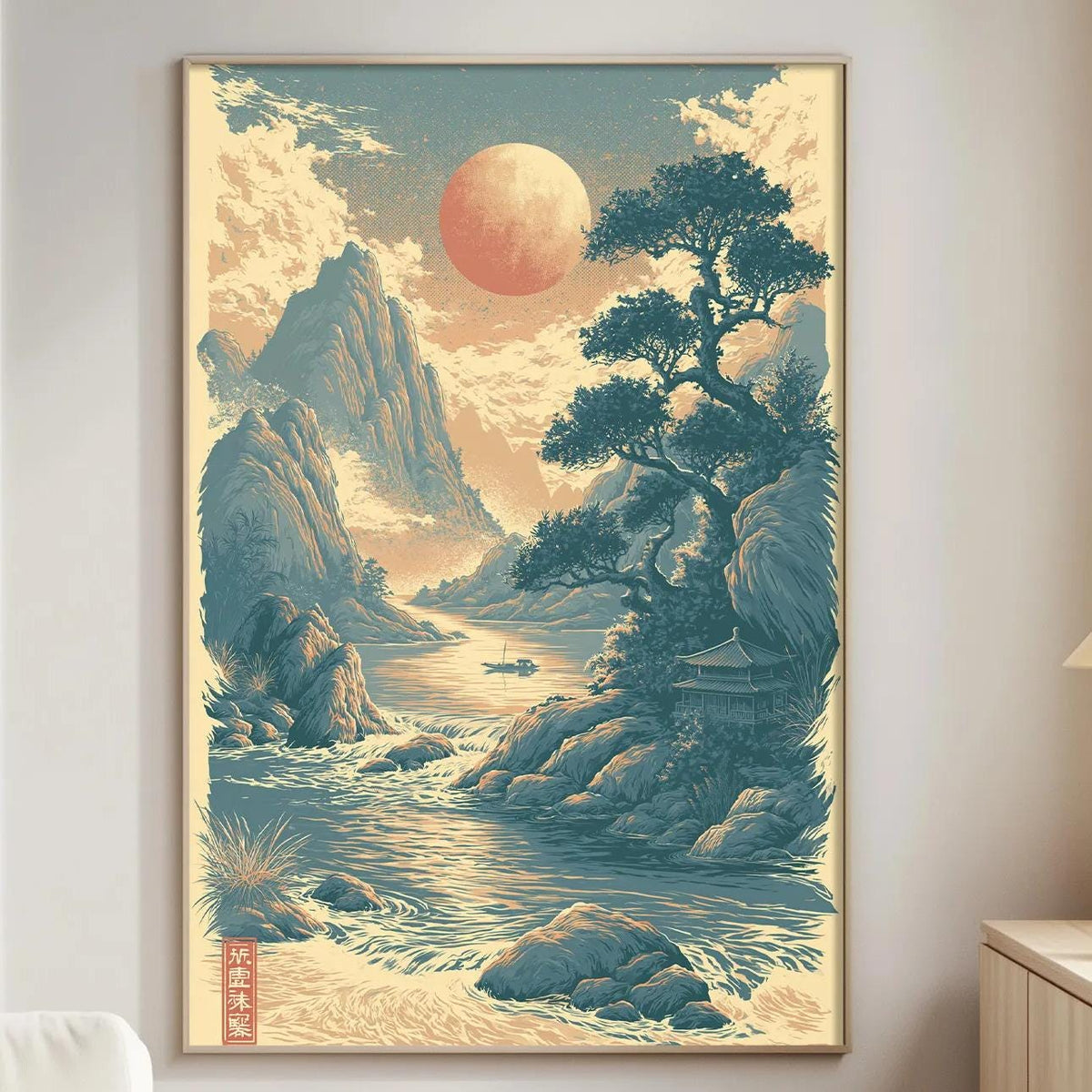 a large framed poster of a serene landscape with mountains, a river, and a large red moon in the sky. The poster is hanging on a wall in a living room setting, with a white couch and a wooden side table nearby.