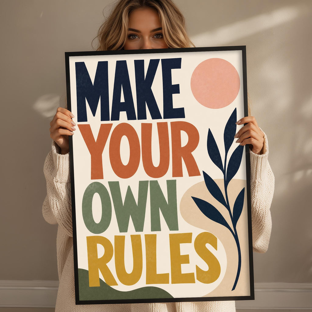 A woman holding a framed poster with the text "MAKE YOUR OWN RULES" on it.