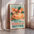 A framed poster with a vibrant illustration of a pie surrounded by autumn leaves and fruits, along with the text "Bake the World Better".
